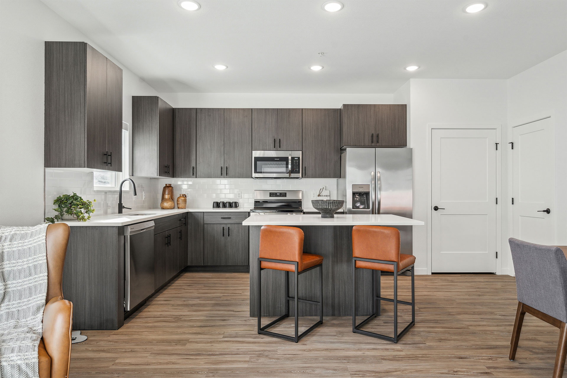 Modern kitchen with dark cabinets, stainless appliances, white countertops, and two orange bar stools