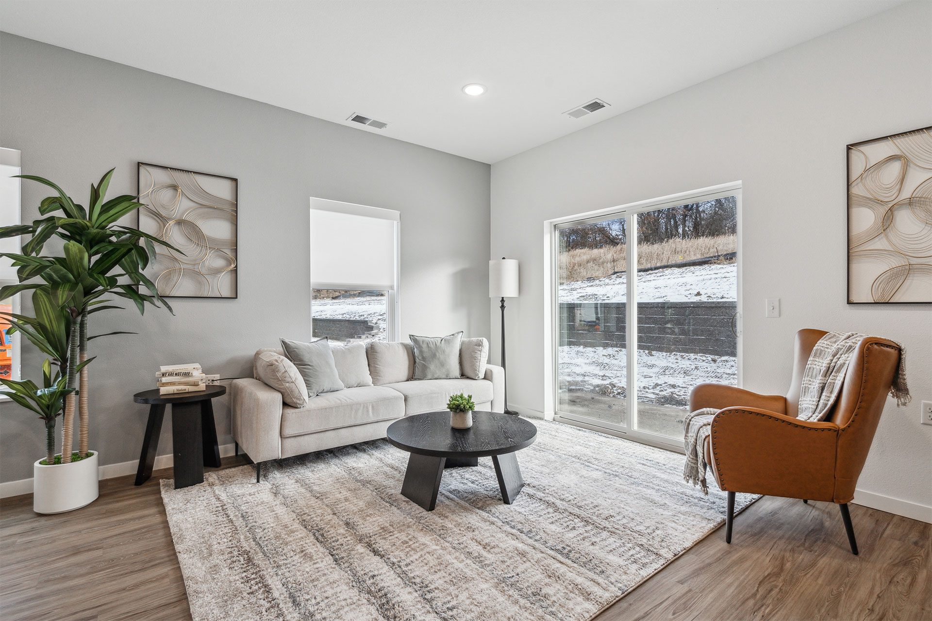 Bright modern living room with a sofa, armchair, coffee table, and large windows overlooking a snowy yard