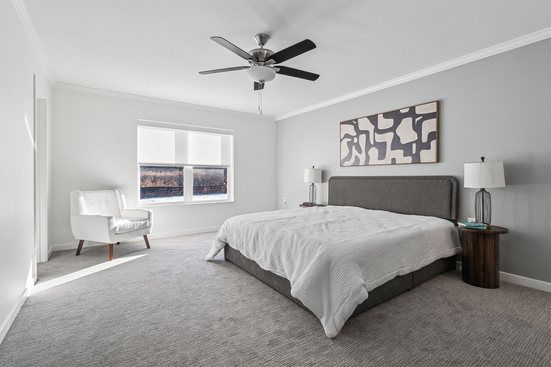 Bright modern bedroom with gray walls, a bed, armchair, and ceiling fan