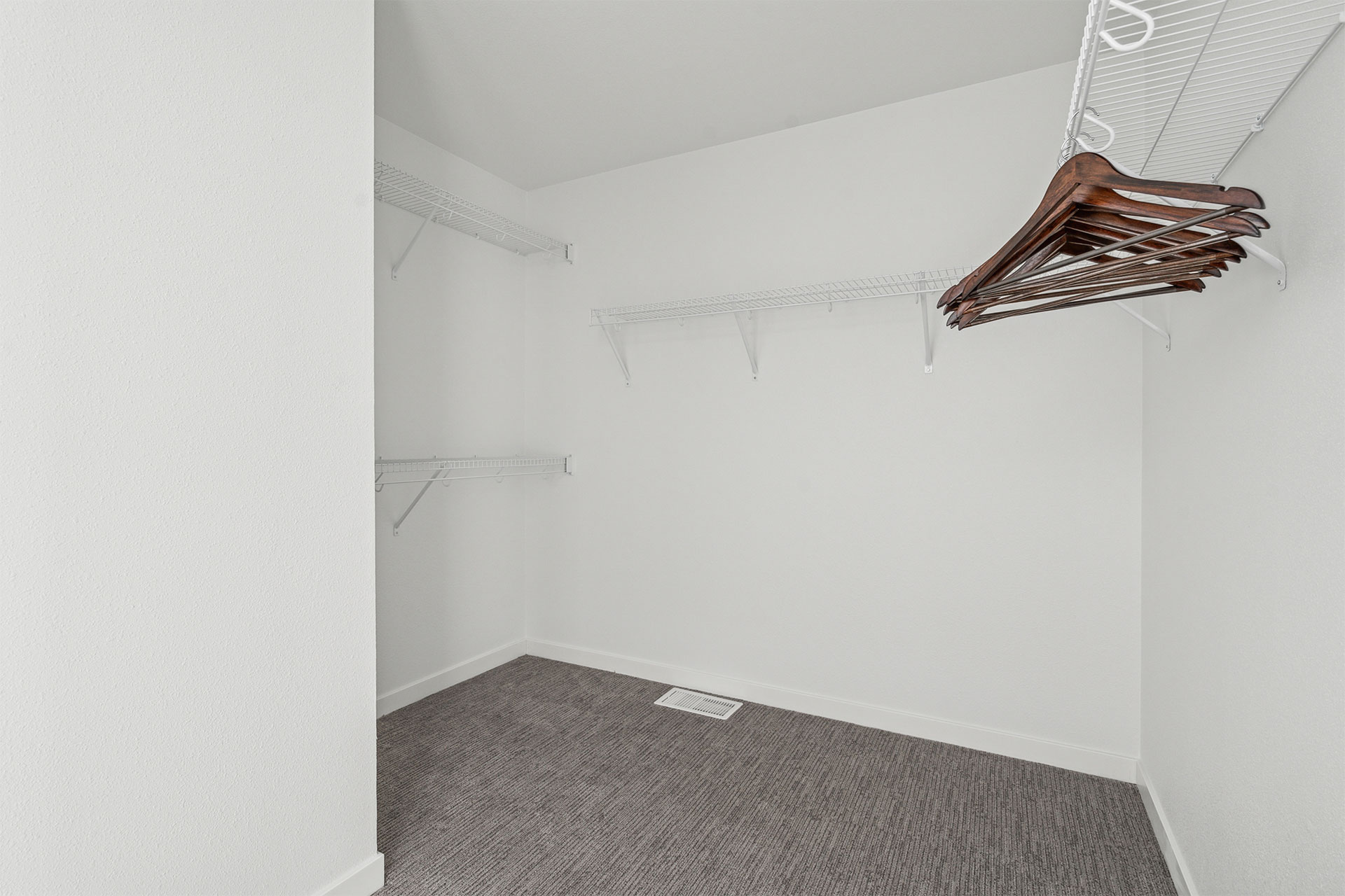 Empty walk-in closet with wire shelves and hanging wooden hangers