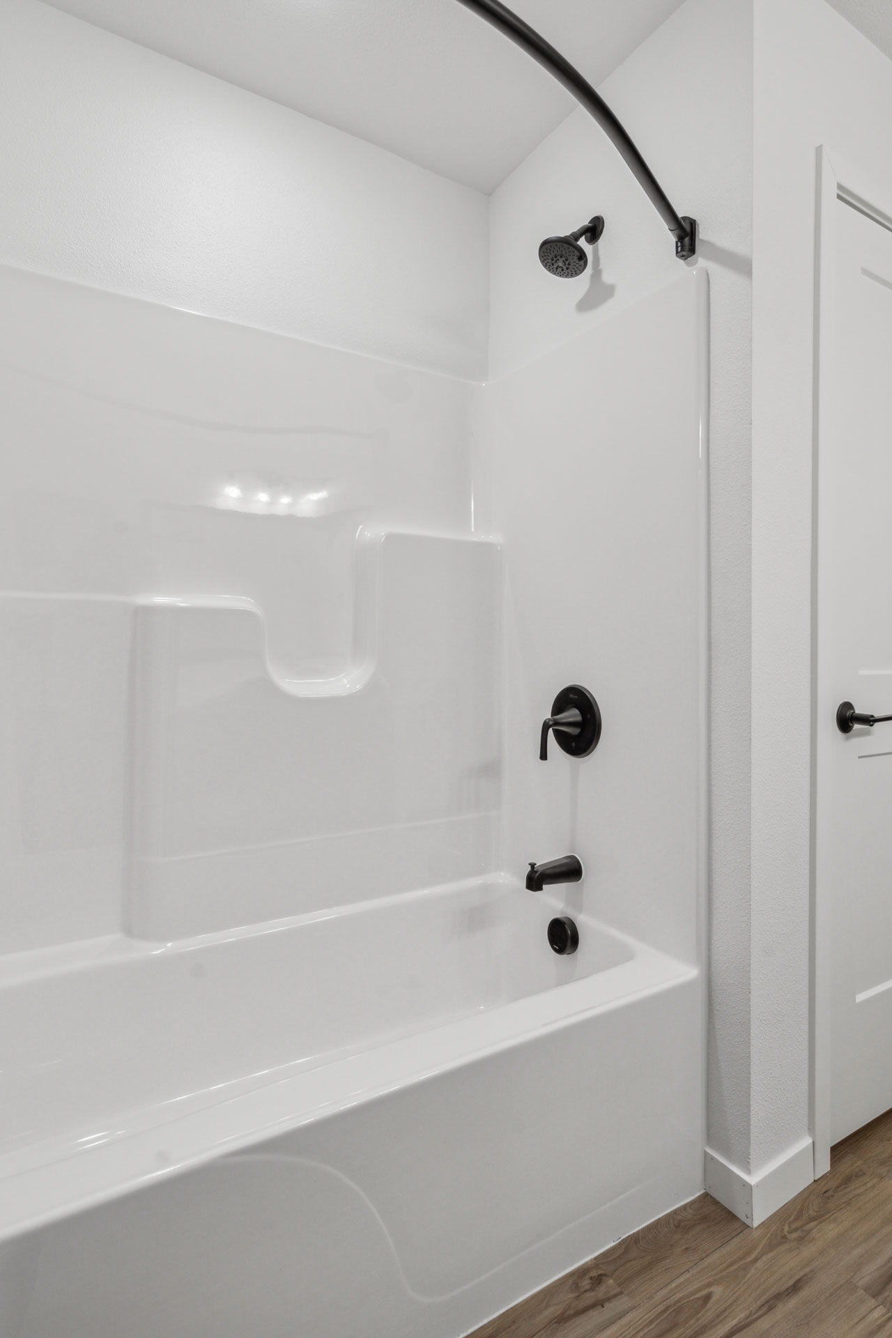 White bathtub and shower with black fixtures in a bathroom alcove